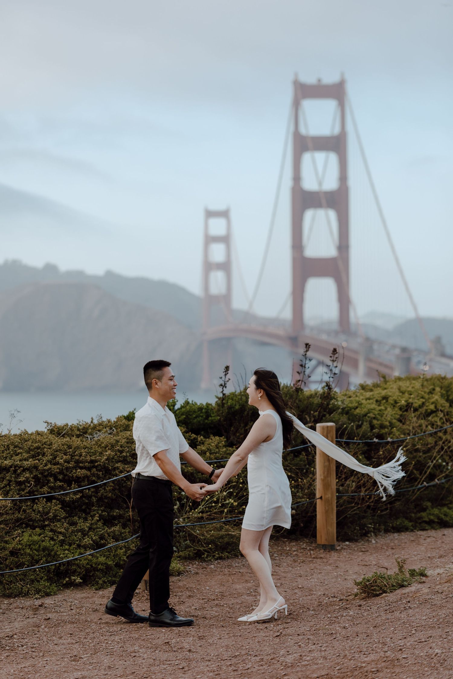 A couple shares a romantic moment at Battery Spencer viewpoint with the foggy Golden Gate Bridge in the background.