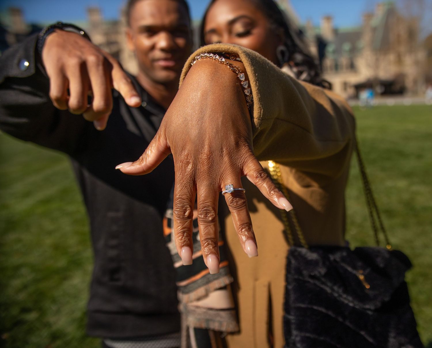Hand outstretched showing decorated fingernails with rings on a sunny day in a grassy park.