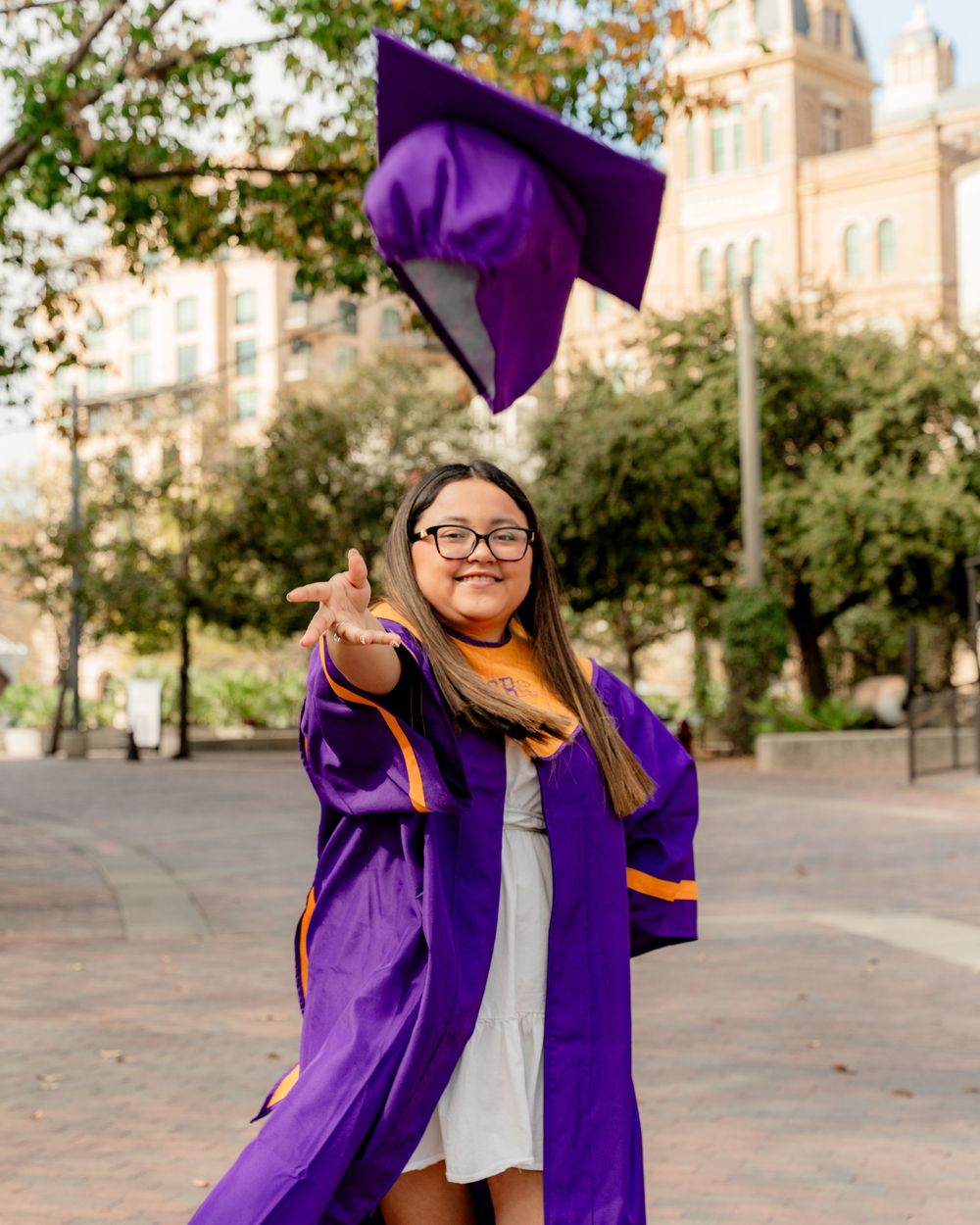 Graduate in purple commencement robes celebrates by tossing cap in front of historic building.