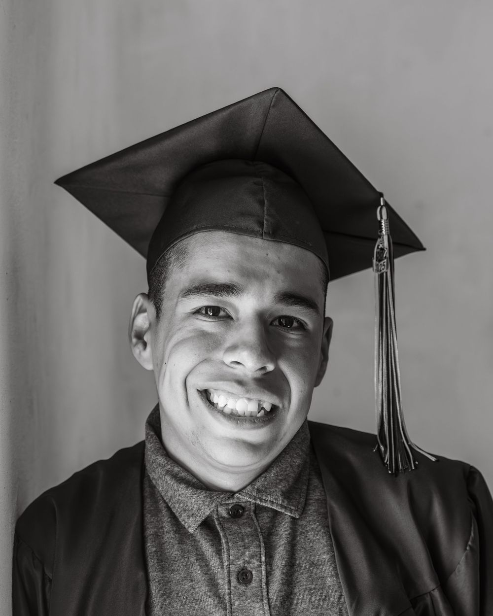 A graduate in cap and gown smiles brightly in black and white portrait.