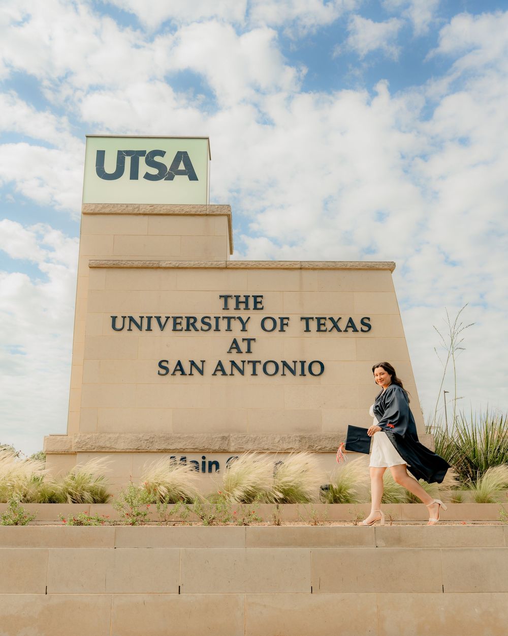 A graduate poses playfully in front of the UTSA sign on campus.