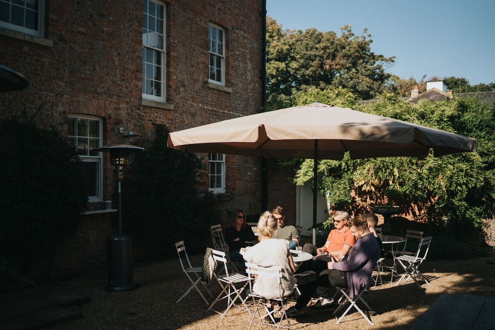 People gathered around tables under a beige umbrella on a brick patio outside a historic building at Aswarby Rectory.