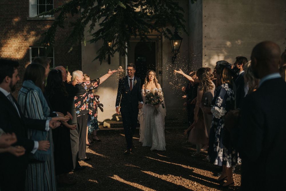 A glowing pathway leads past dark buildings as people gather in small groups during an evening event at Aswarby Rectory.