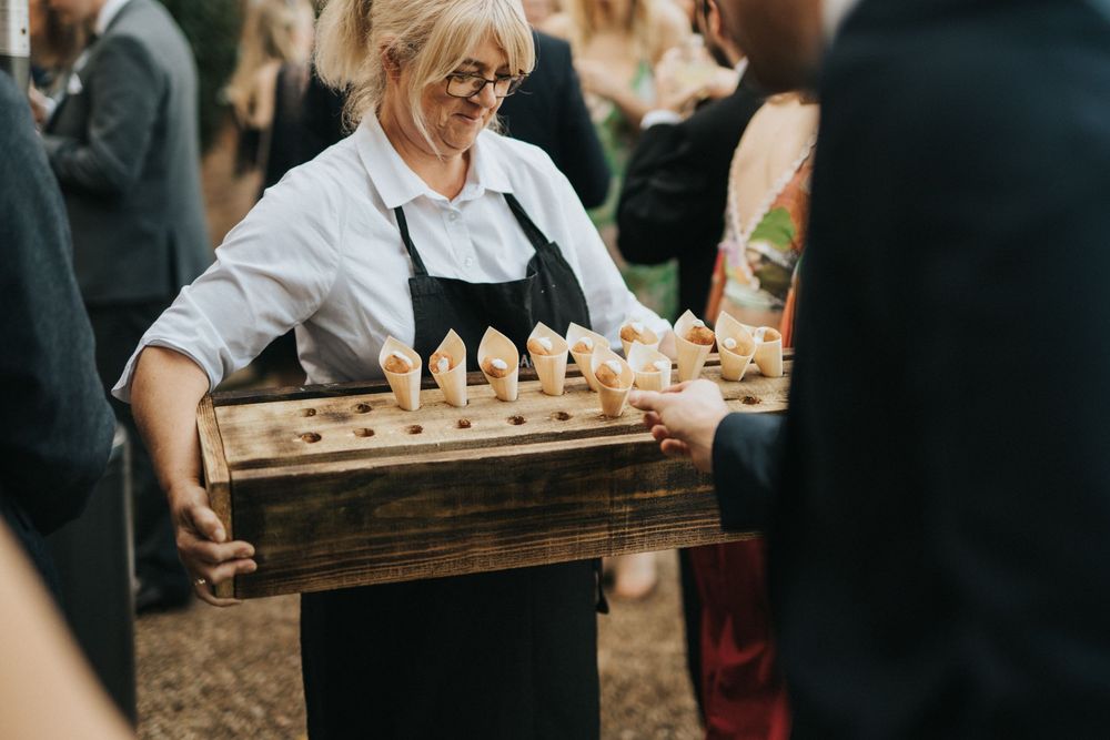 Server presents a wooden tray of dessert cones at an outdoor wedding event at Aswarby Rectory.