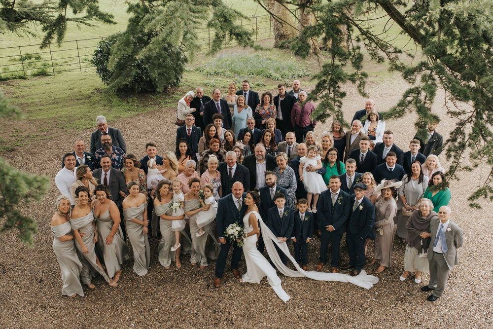 Large wedding party gathered outdoors for a group photo under tree branches on a sunny day at Aswarby Rectory.