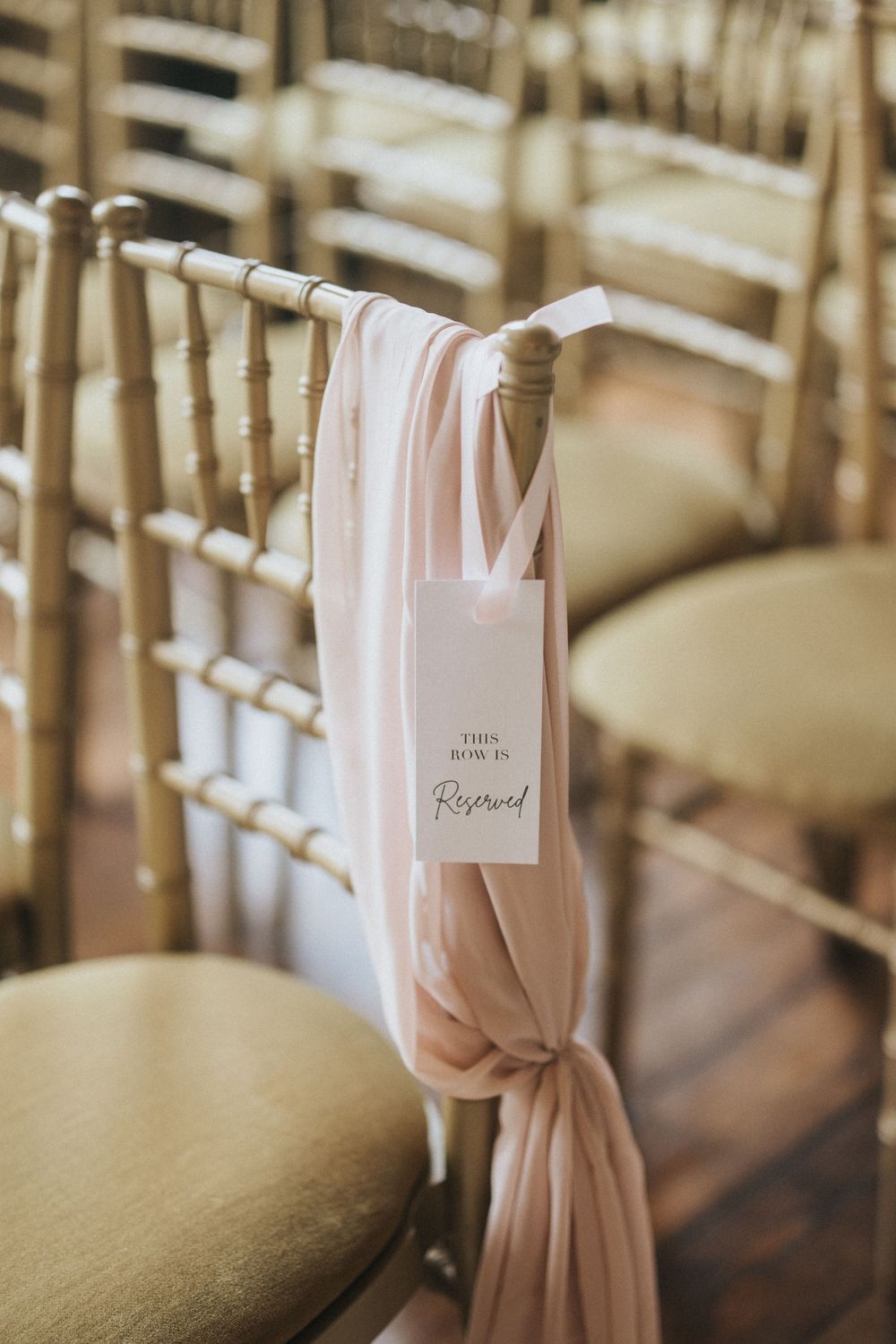 Elegant pink sash tie decorations on bamboo wedding ceremony chairs with name cards creating a romantic aisle setting at Rise Hall.