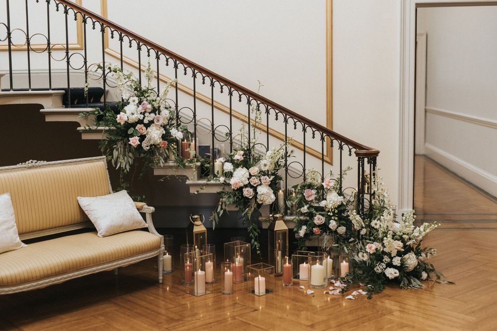 Elegant staircase with white and gold railing adorned with white floral arrangements in luxurious interior settings at Rise Hall.