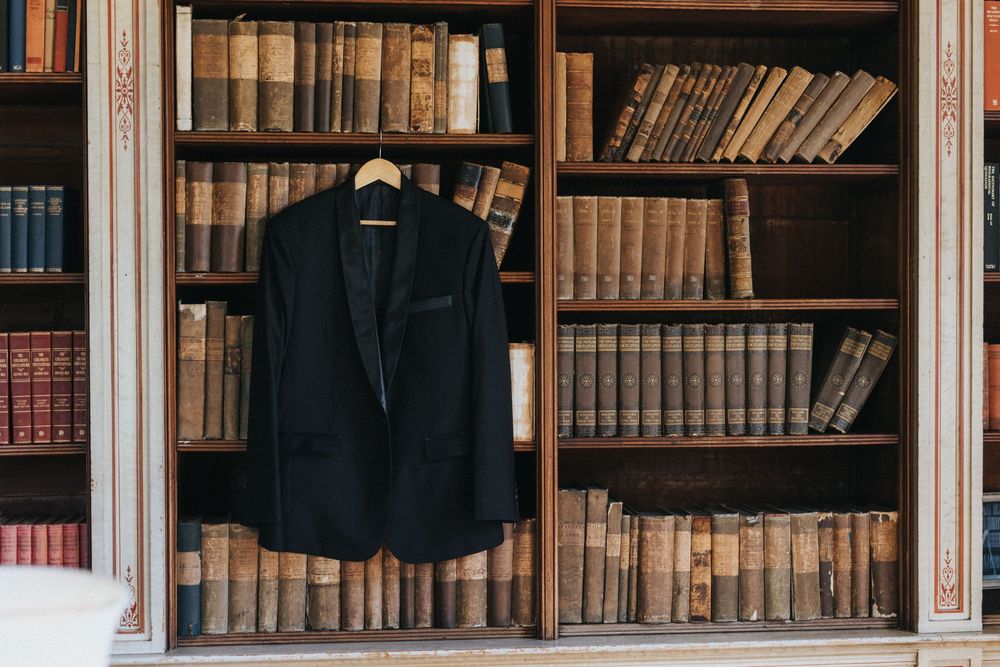 A black blazer hangs in front of vintage wooden bookshelves filled with antique leather-bound books at Rise Hall.
