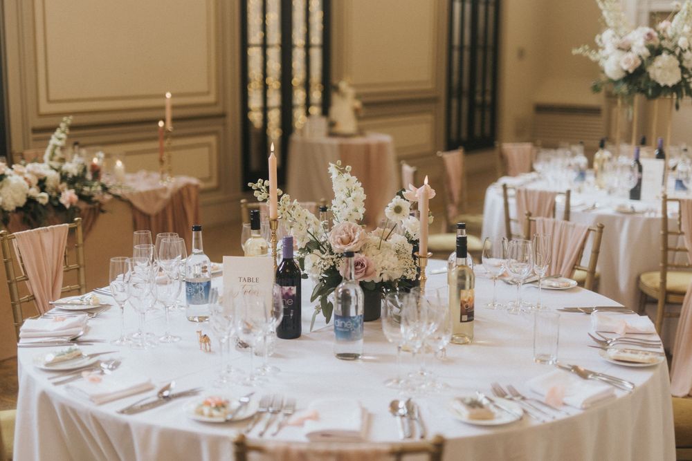 Elegant wedding reception venue with round tables set with white linens and crystal glassware in a grand ballroom at Rise Hall.