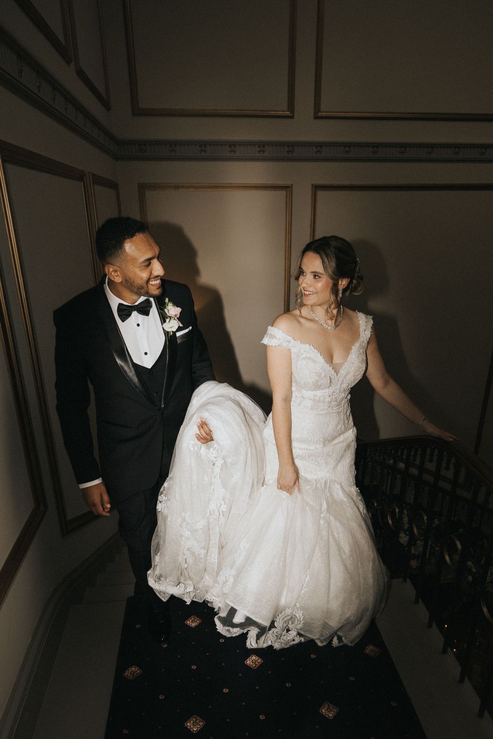 A newlywed couple share a sweet moment while walking up an elegant staircase at Rise Hall.