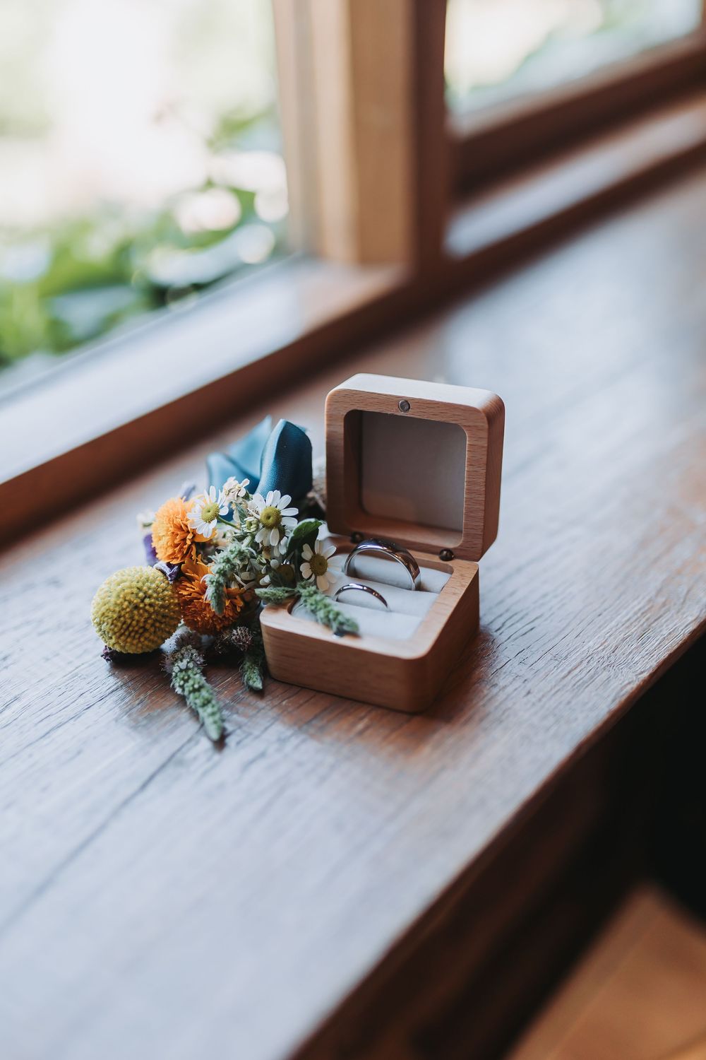 Small brown ring box with dried flowers and greenery on a wooden window ledge.