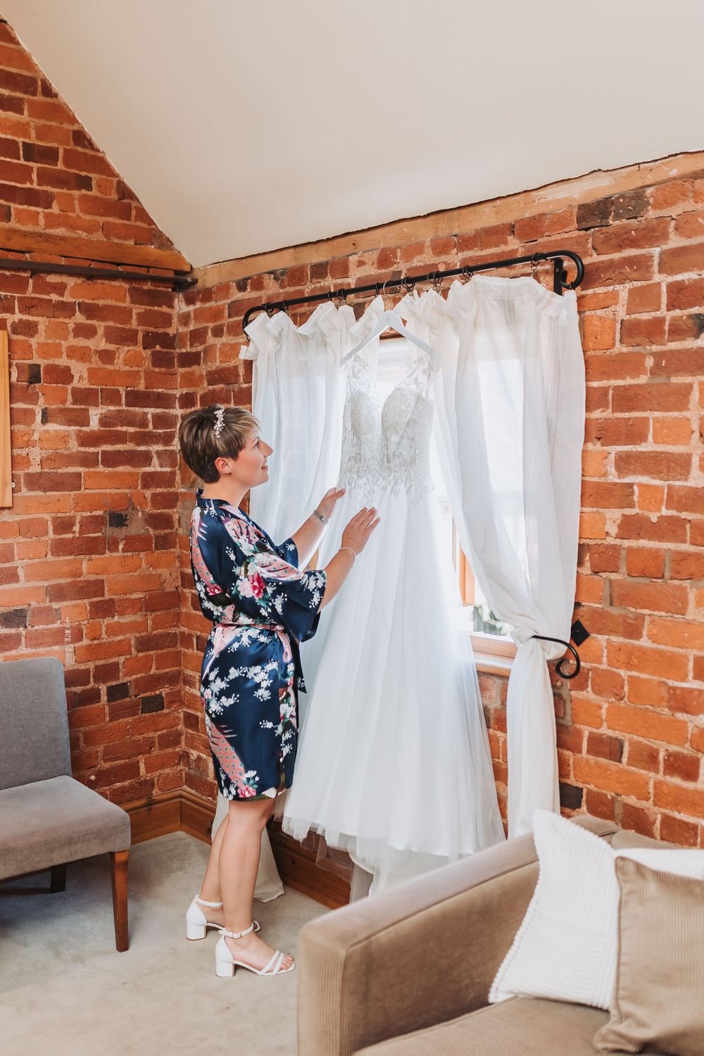 A white wedding dress being hung on a curtain rod against an exposed brick wall.