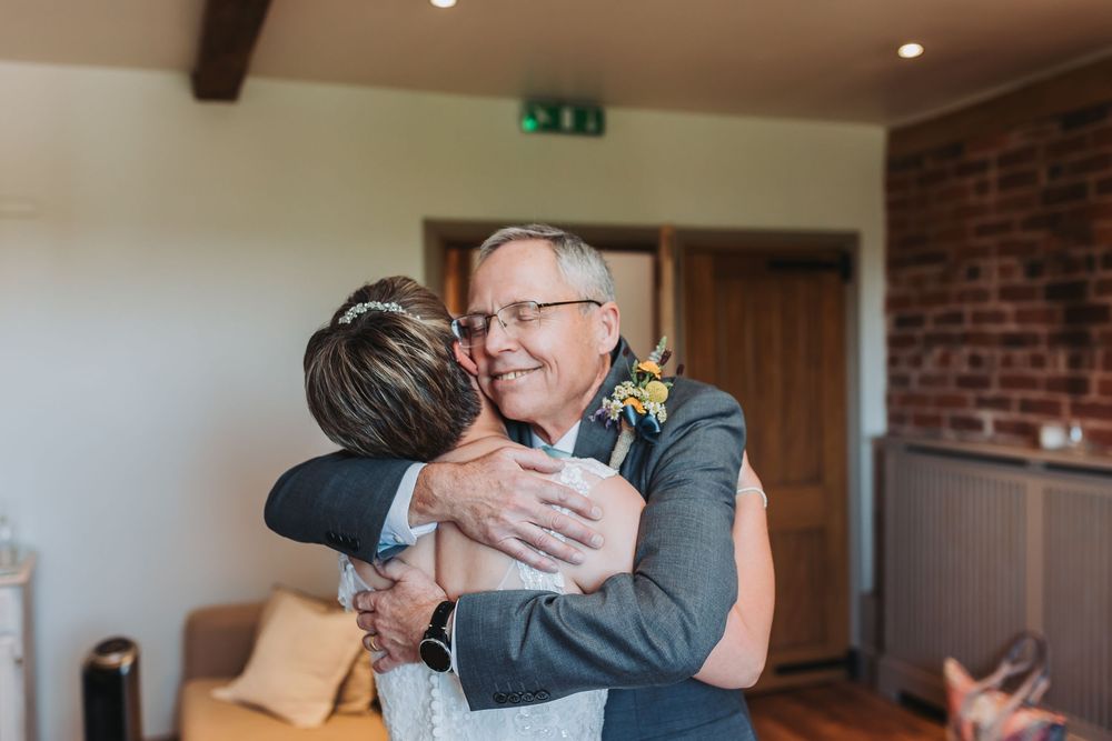 Two figures embracing in an indoor setting with natural light streaming through windows.