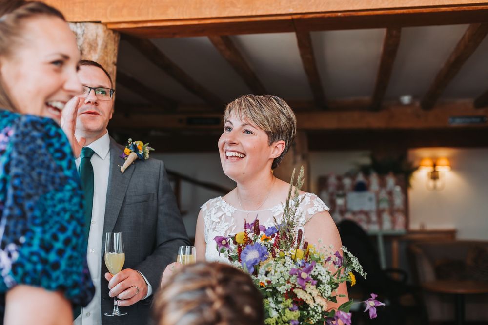Candid moment at a rustic reception venue with natural light streaming through windows and floral decorations.