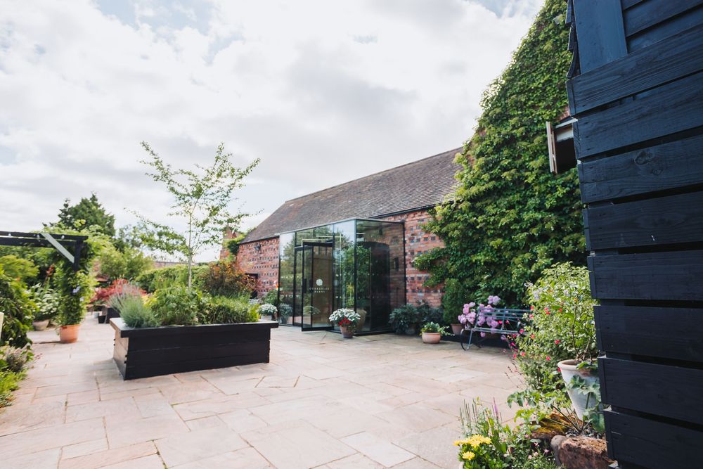 Modern glass-walled extension connecting to traditional brick building with landscaped garden patio and planters.