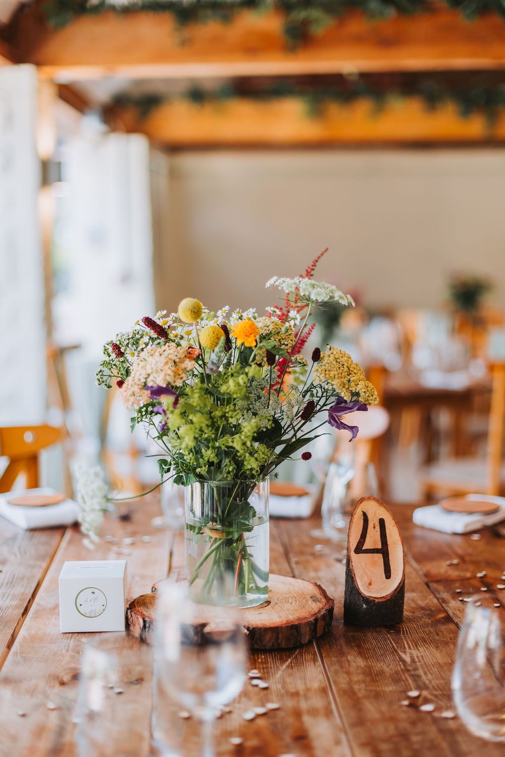 Rustic wedding table decor with wildflower centerpieces in glass jars set on wood slices with table numbers.