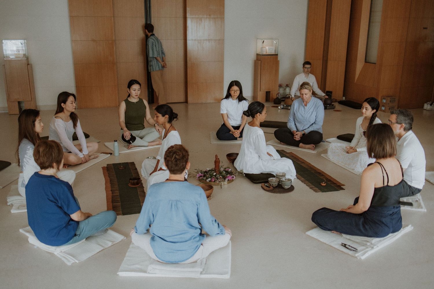Students sit on yoga mats during a wellness class in a studio with wooden walls.