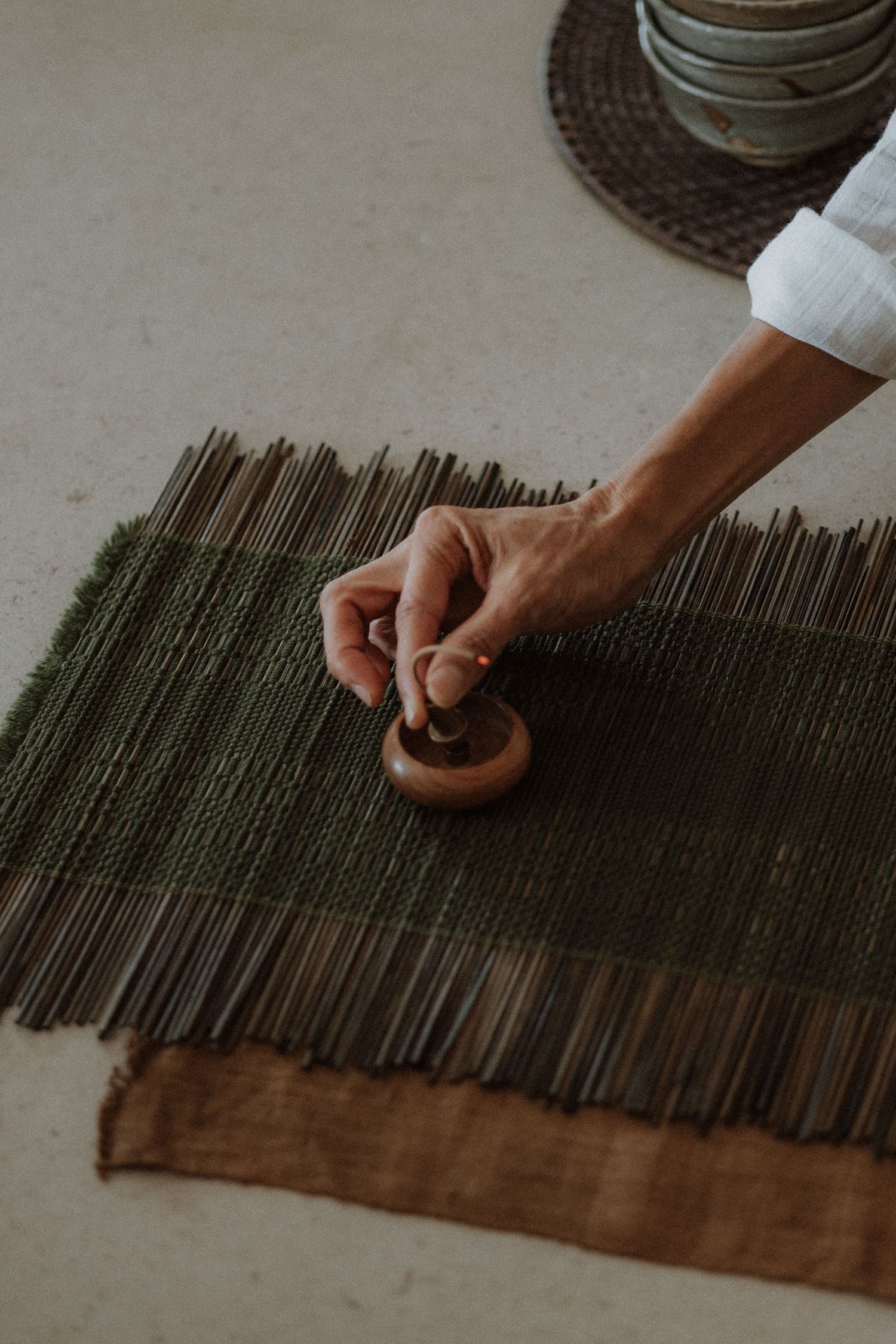 Hands are shown meticulously arranging dark thin bamboo sticks in parallel rows on a brown textile surface.