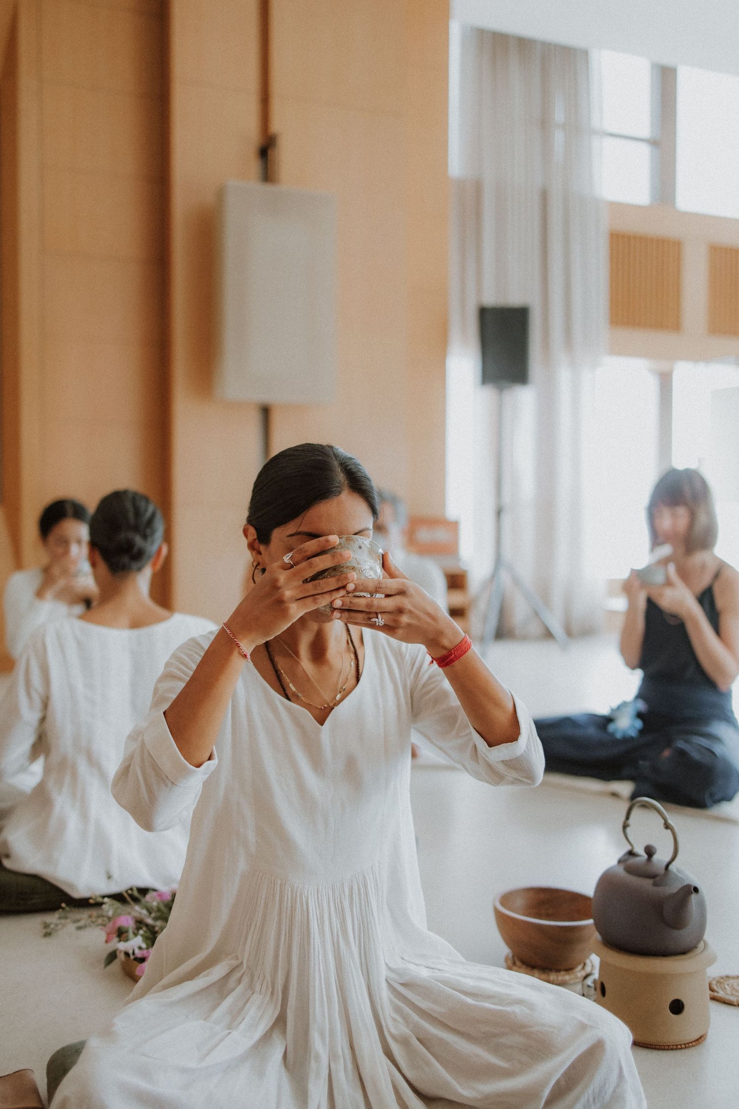 A person in a flowing white dress drinks from a tea bowl during a mindful ceremony practice.