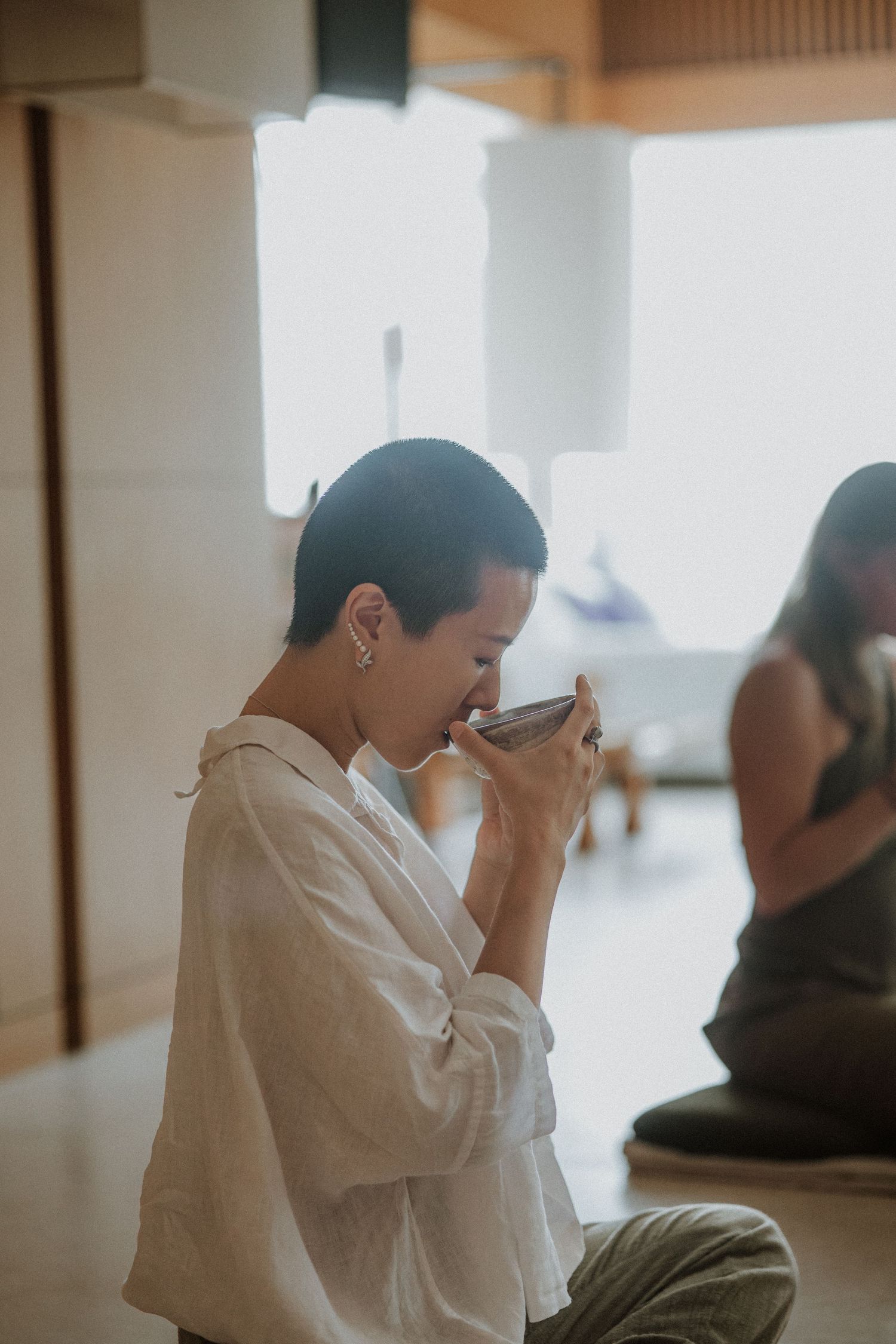 Person in white clothing sits in contemplative pose at what appears to be a meditation or spiritual gathering space.