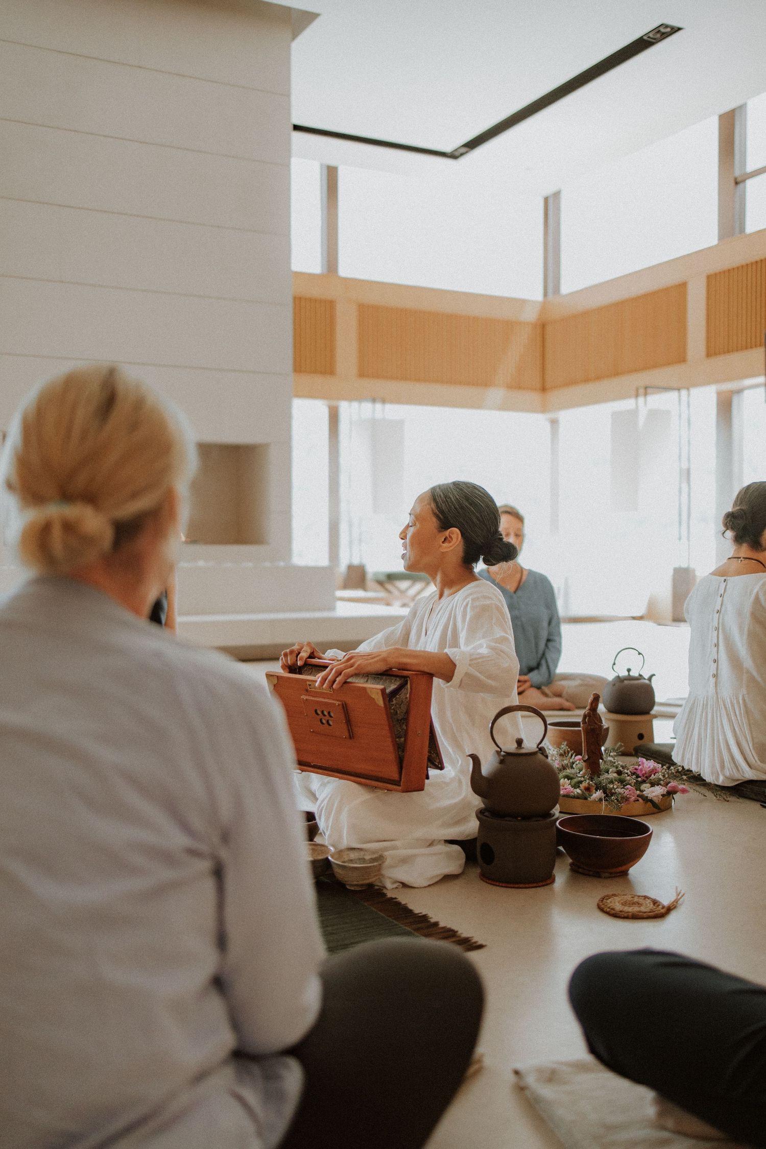 A group of people gather in a bright, minimalist space for a traditional tea ceremony with cast iron teapots.