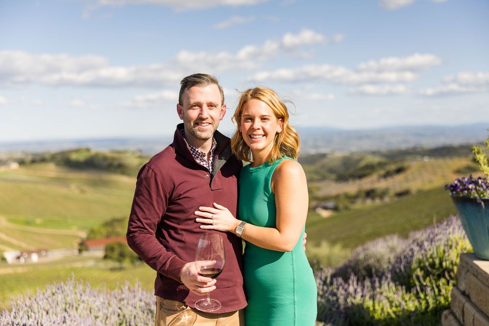 Couple standing together on a scenic hilltop overlooking rolling Tuscan countryside on a sunny day.