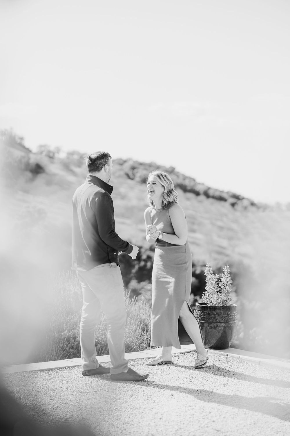 A couple stands together on a hilltop in black and white as they share an intimate moment during a marriage proposal.