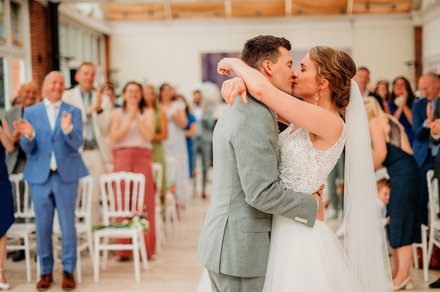 Bride and groom share their first dance surrounded by cheering guests in a bright rustic venue.