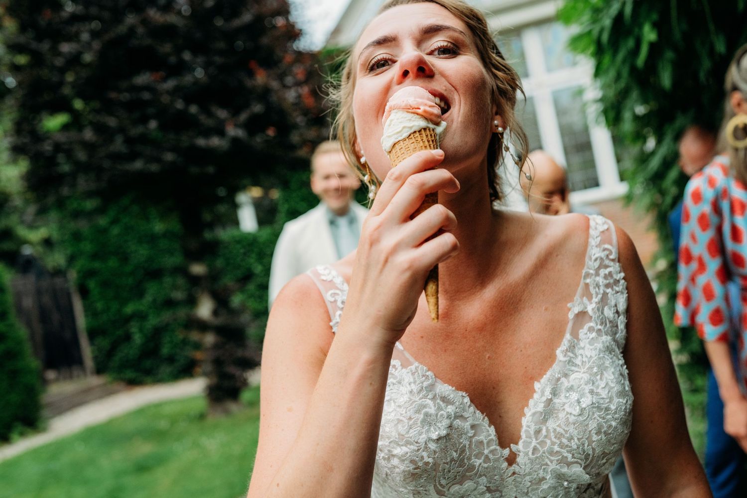 Someone in a white sequined dress enjoys an ice cream cone while standing in a garden on a sunny day.