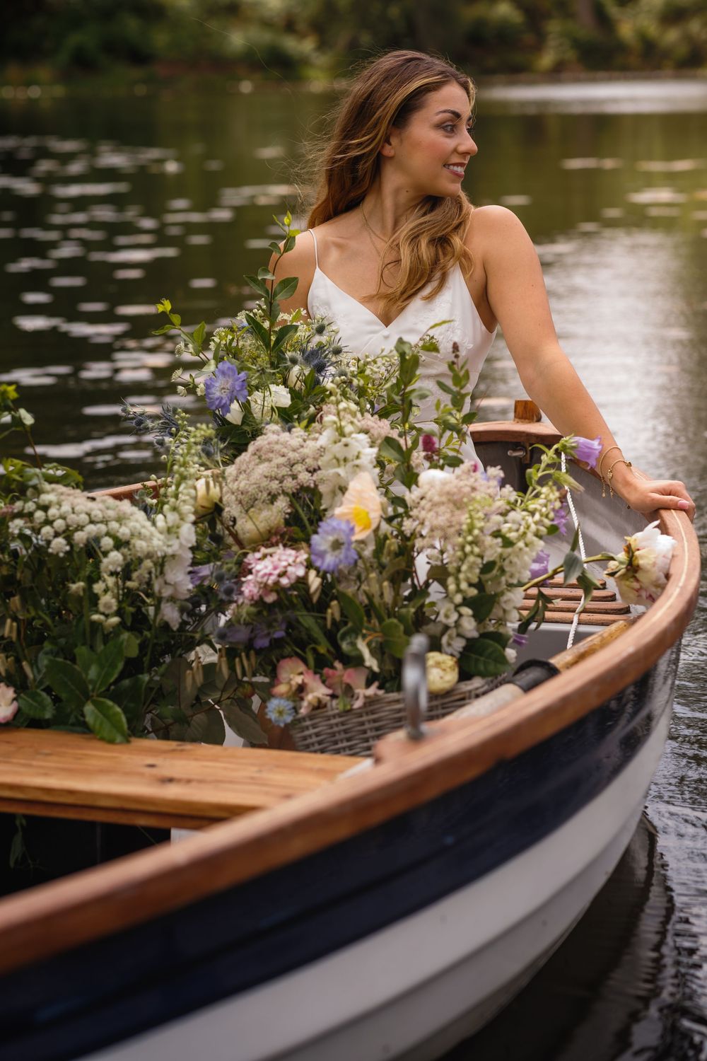 A decorated wooden canoe filled with fresh floral arrangements glides across a peaceful pond.
