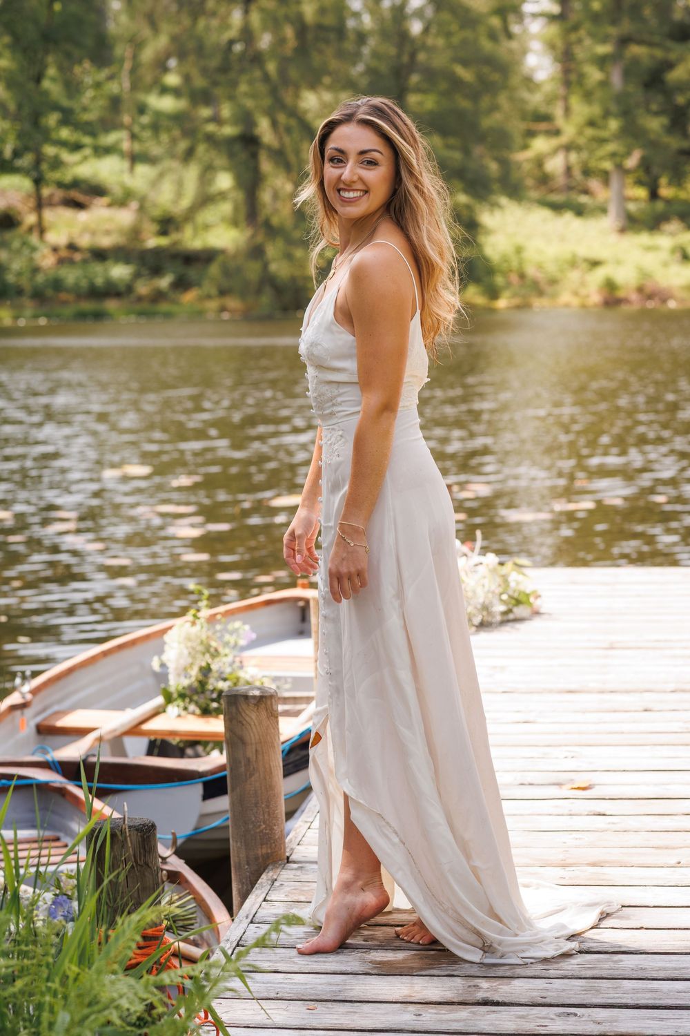 A white wedding dress and wooden dock create a romantic lakeside portrait with a boat in the background.