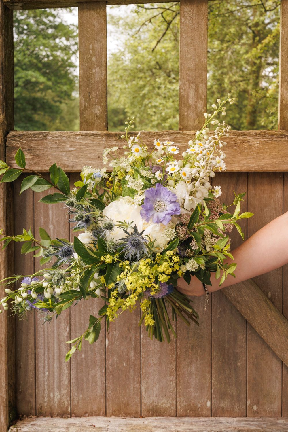 A rustic wooden backdrop frames a beautiful wedding bouquet with purple and white flowers.