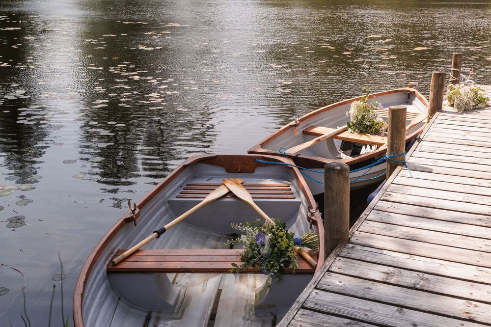 Wooden rowboats tied to a dock with wedding flowers placed inside.