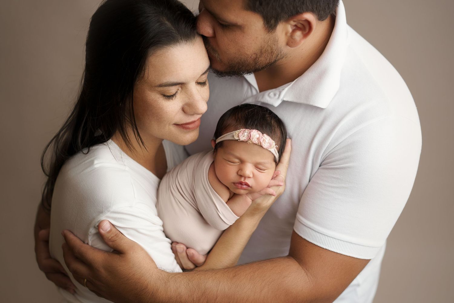 Tender family maternity portrait in neutral tones against brown background.
