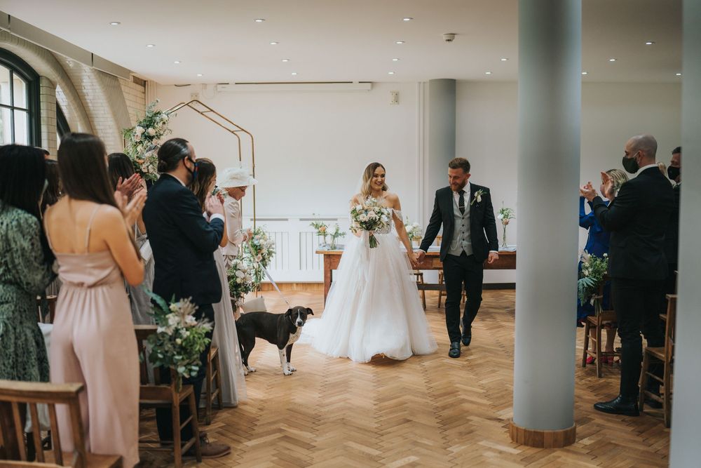 A panoramic view of a modern white wedding venue space with guests mingling and a turquoise support column.