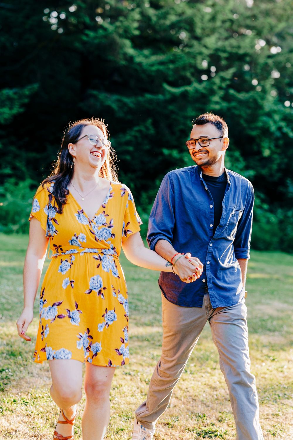 A couple walks hand in hand through a sunny field wearing coordinated casual outfits.