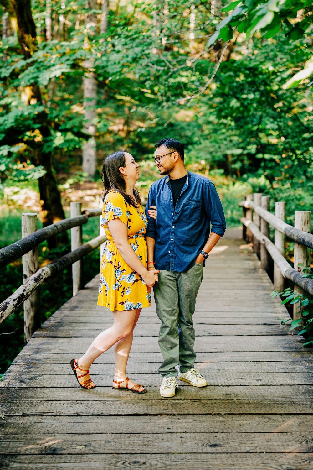 Couple shares playful moments on a rustic wooden footbridge surrounded by lush green forest.