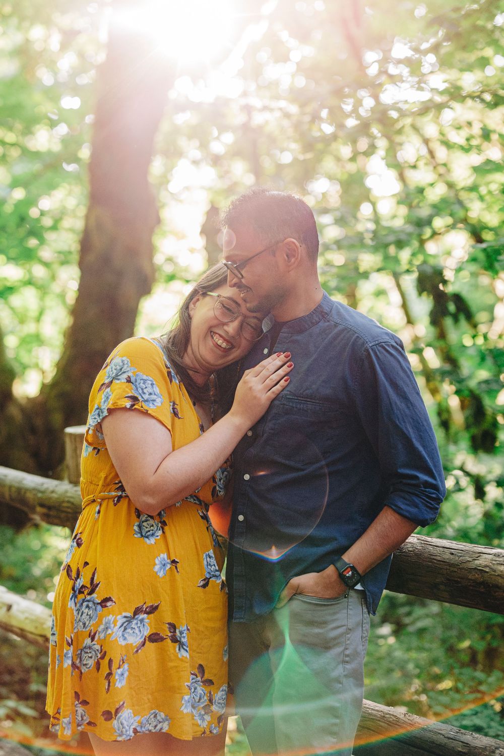 A romantic couple shares an intimate moment leaning against a wooden fence in a sunlit outdoor setting.