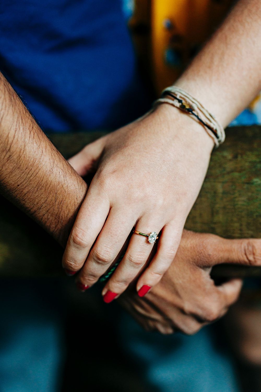 Close-up of hands touching with one hand wearing a bracelet and diamond engagement ring with red nail polish.
