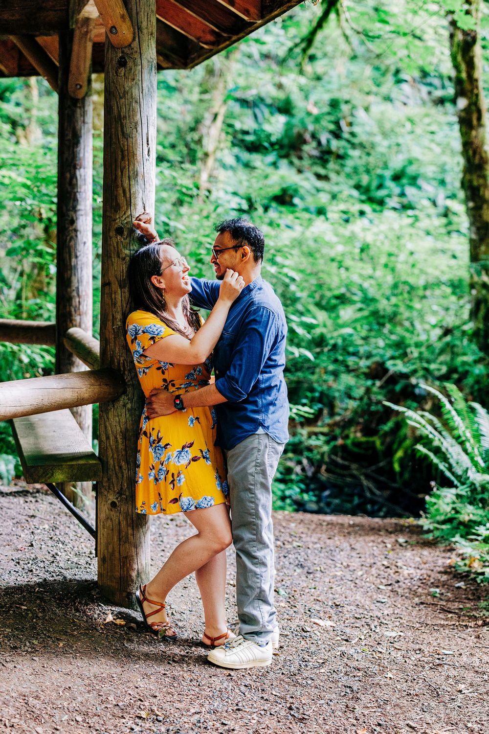 A couple shares a romantic moment in a rustic wooden gazebo surrounded by lush green forest.