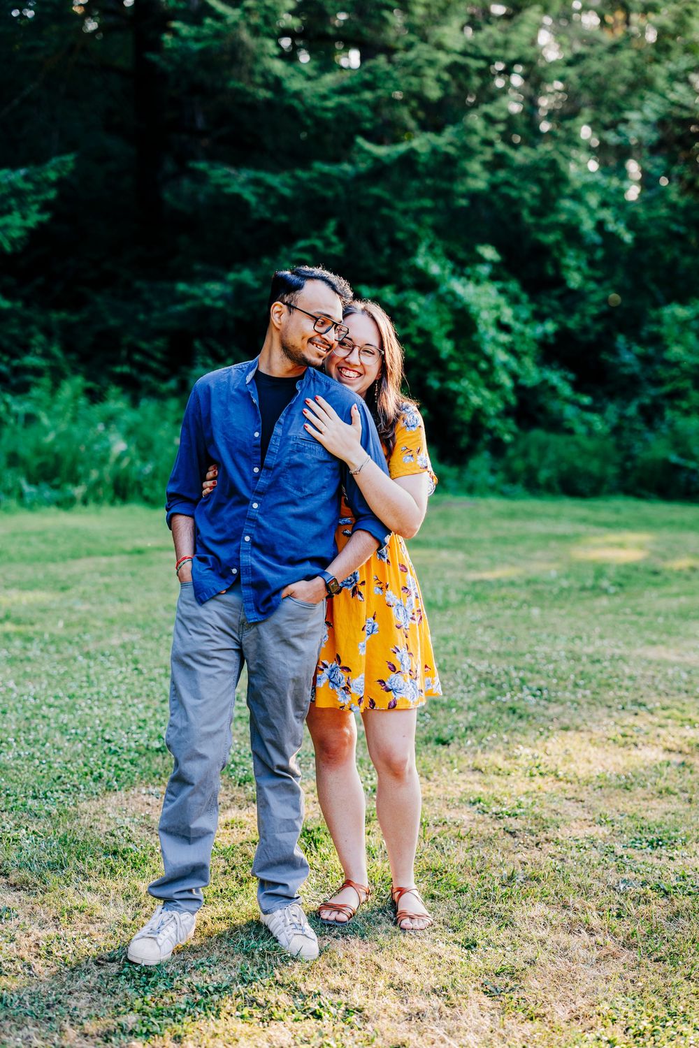 A couple stands together on grass with trees in background, wearing coordinating blue and yellow outfits.