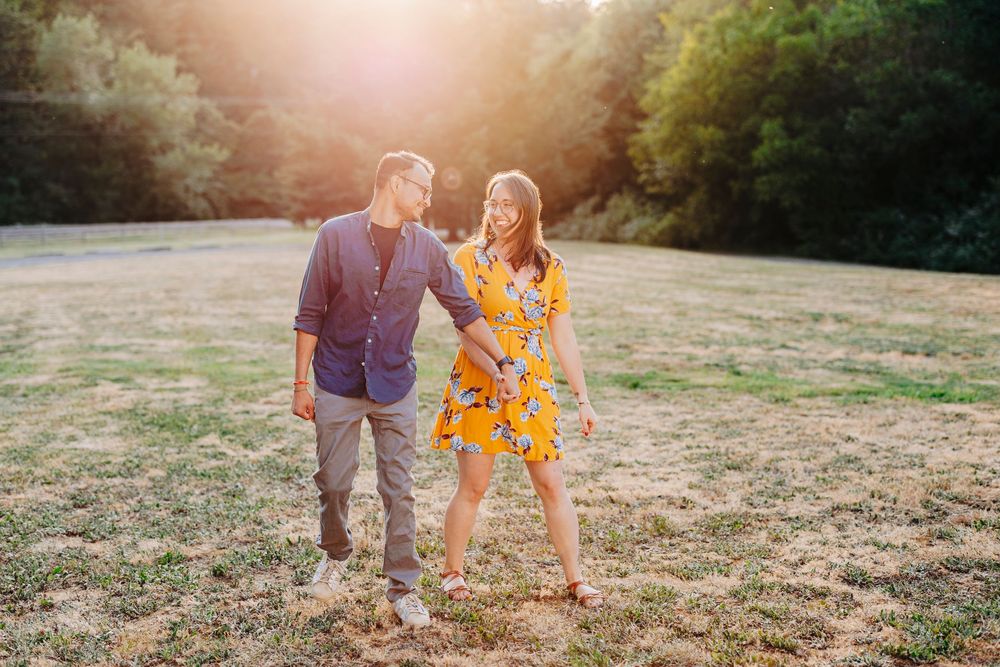 A couple in casual attire walking together on a rustic dirt path during sunset creates a romantic outdoor scene.