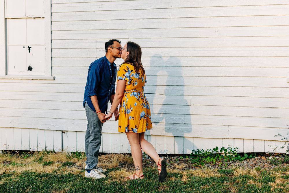 Two people share a tender embrace and lean in for a kiss against a white painted wall.