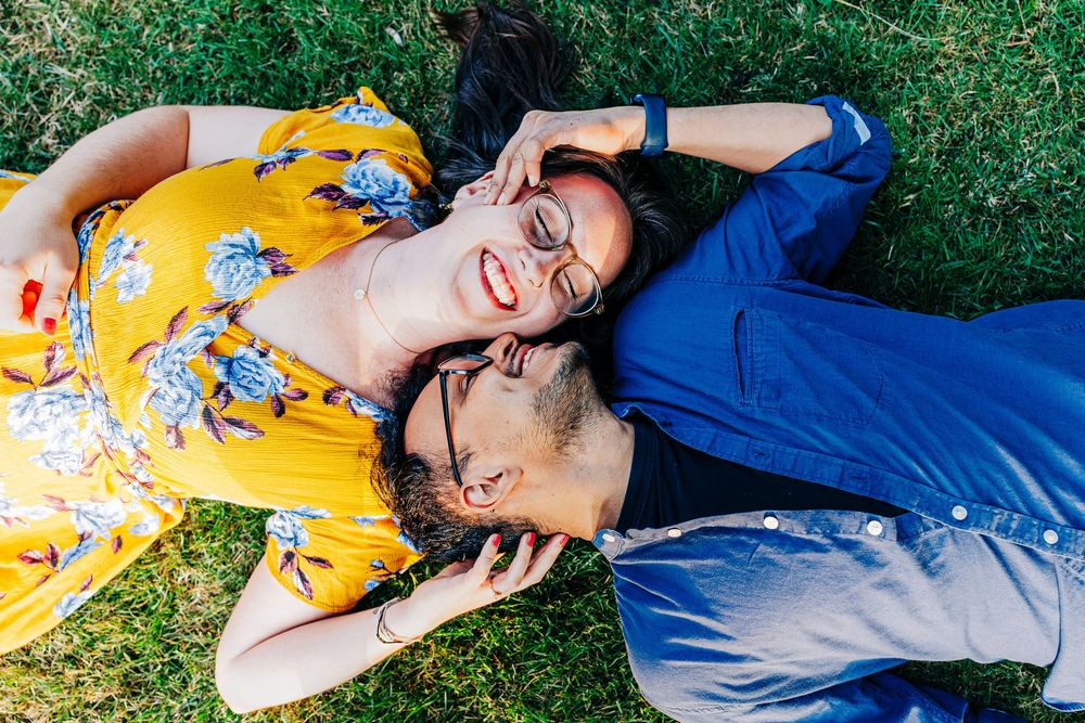 A couple in yellow and blue outfits laying in grass while sharing a joyful moment together.