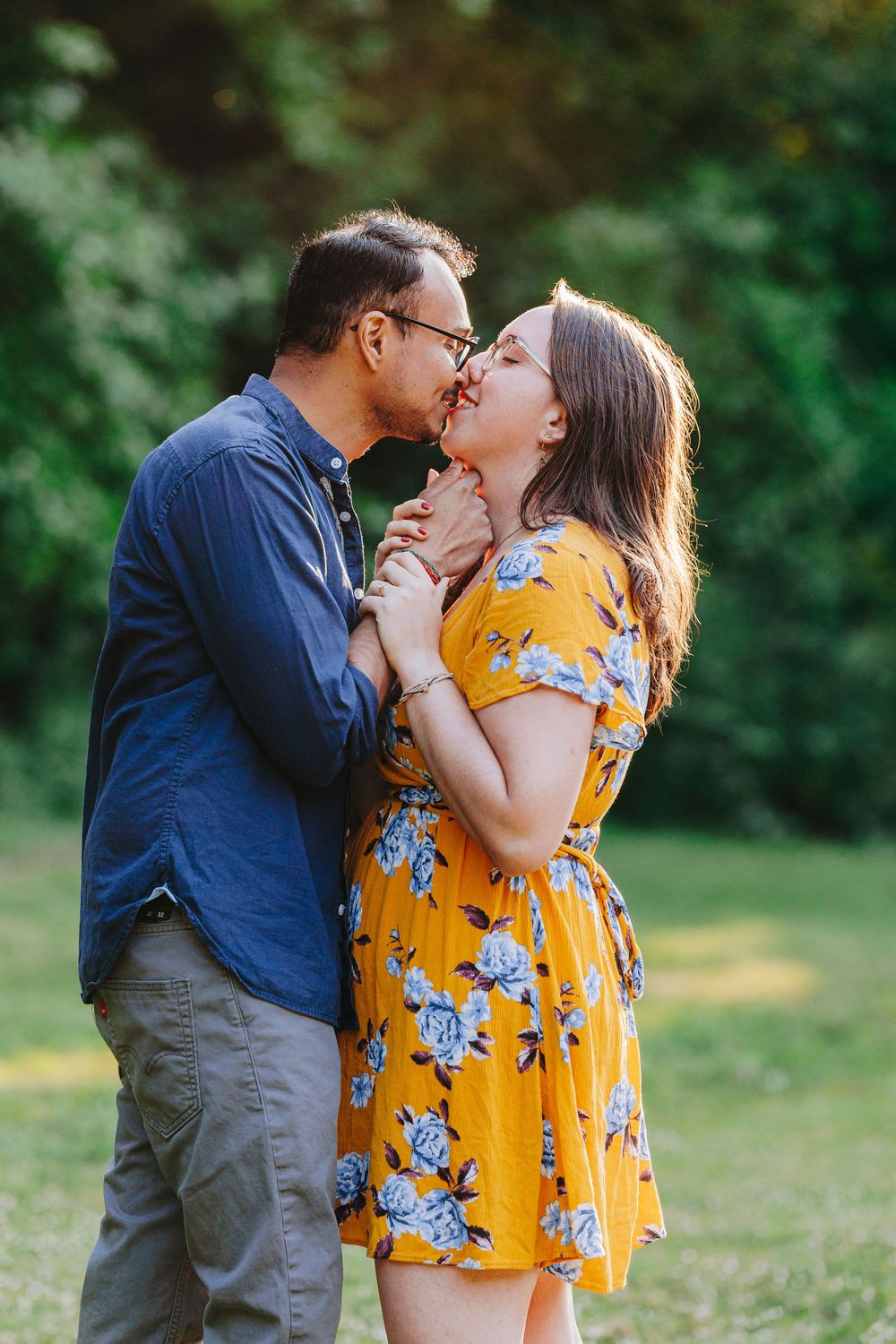 Tender embrace between a couple in a park, with woman wearing bright yellow floral dress.