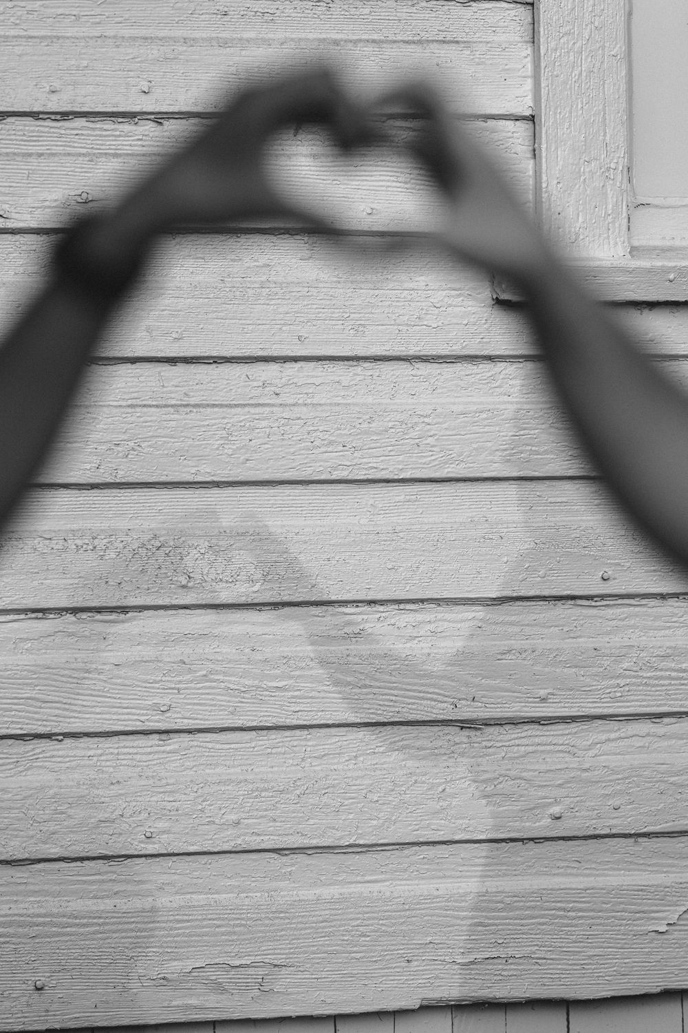Hands form a heart shadow against white wooden siding outdoors.