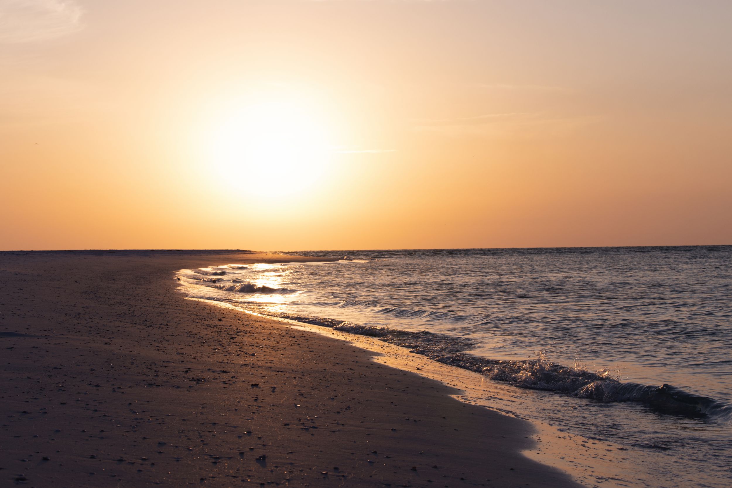 A golden sunset illuminates a peaceful beach shoreline with gentle waves rolling onto the sand.