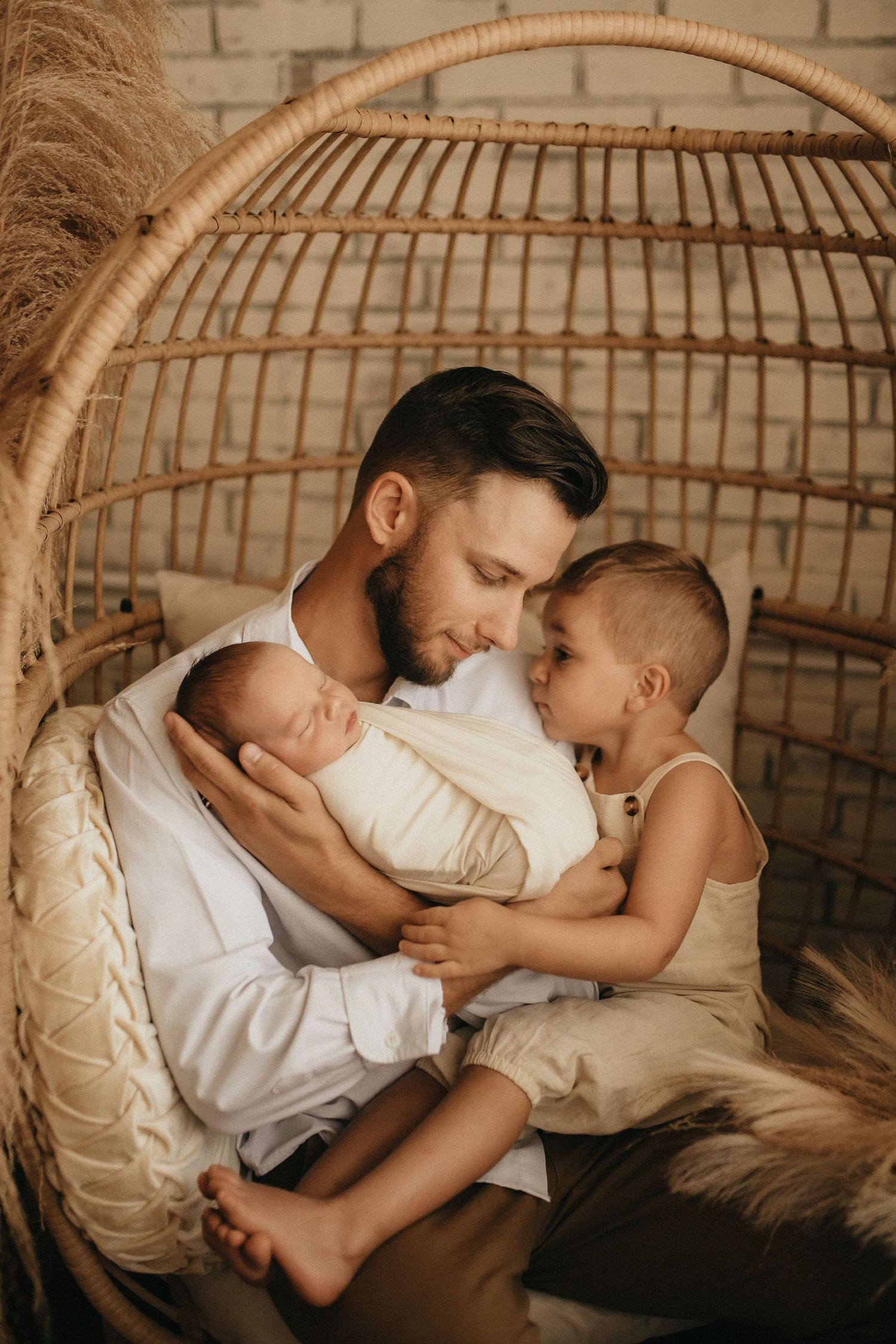 warm family photo in a boho studio of a father holding his infant newborn while smiling at his toddler