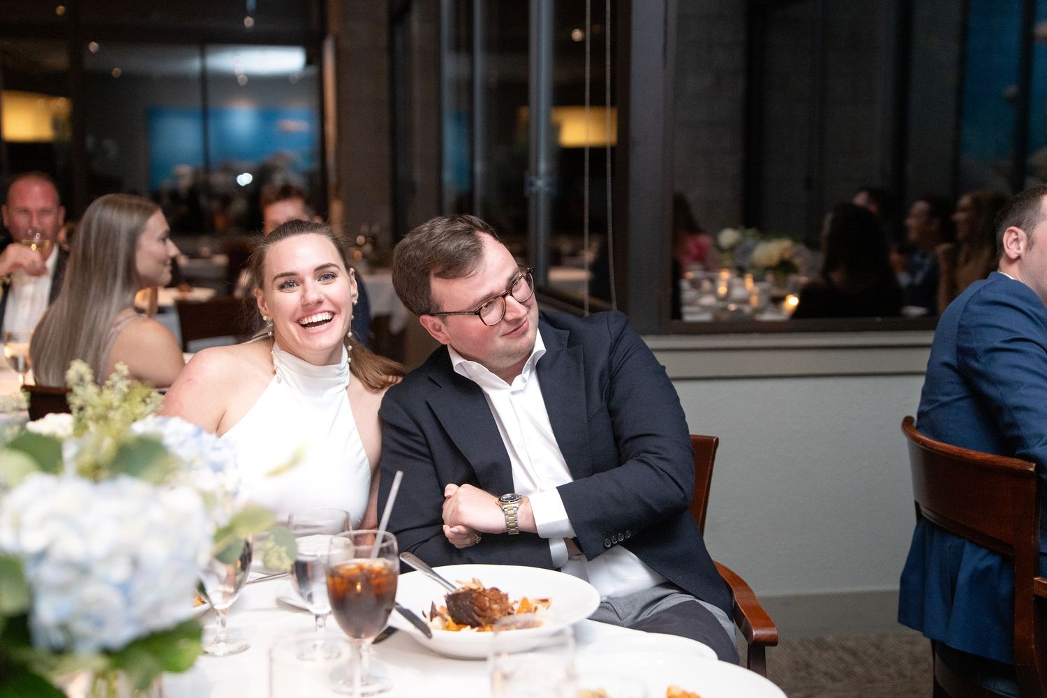 Vibrant wedding reception scene with people dining and celebrating at elegantly decorated tables in an indoor venue.