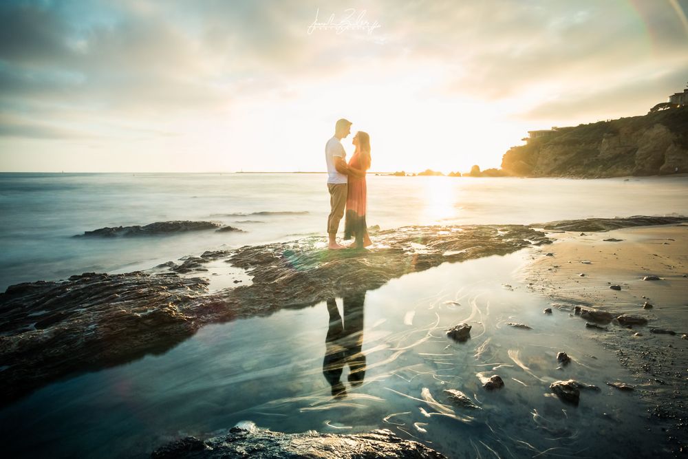 Silhouetted couple standing on rocky beach at sunset with reflection in the little corona del mar tidal pools.
